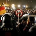 people-attending-an-anti-immigration-demonstration-organised-by-pegida-walk-past-opponents-of-pegida-behind-police-cars-in-dresden