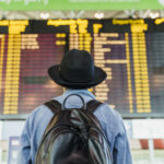 young-man-with-hat-and-backpack-looking-at-arrival-departure-board-at-the-airport