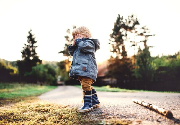 a-little-toddler-boy-standing-outdoors-on-a-road-at-sunset-covering-his-eyes